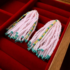 Handmade beaded tassel earrings with pink seed beads and gold accents on a red velvet display