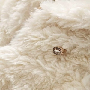 Close-up of soft cream faux fur texture with a metallic buckle on a hooded jacket