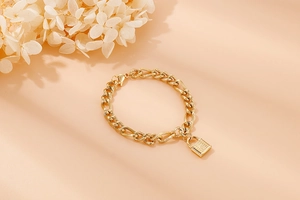 Detailansicht eines goldenen Gliederkettenarmbands mit poliertem Schlossanhänger und Textur