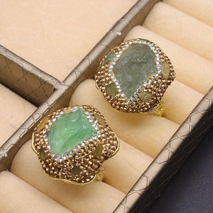 Detail shot of two gold rings with green raw gemstones in a velvet jewelry box