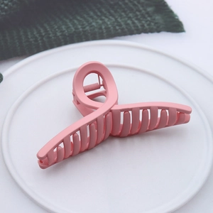 Pink matte finish cross claw clip for women on a white textured ceramic display plate