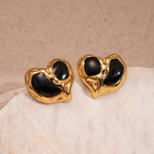 Detailed close-up of heart-shaped gold earrings with black enamel inlay on white stone