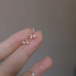 Delicate gold cherry stud earrings with cubic zirconia held on a finger for size