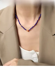 Detail of blue faceted bead necklace with red gold-patterned charm on model