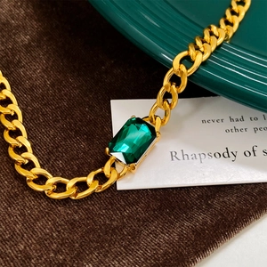 Macro shot of gold chunky Cuban chain with emerald cut green zircon stone detail