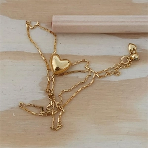 Flat lay of a gold heart pendant necklace on light wood background with fine chain