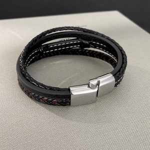 Close-up of multilayer leather bracelet featuring black woven cords and steel magnetic clasp