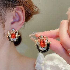Close-up of vintage gold earrings with red gems and black enamel on a female model