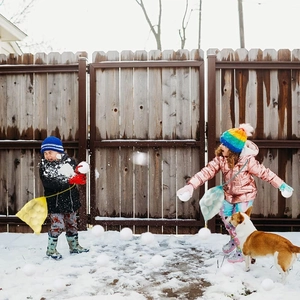 Kids playing with soft snowballs and storage nets in a snowy yard with a dog