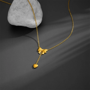Minimalist gold necklace with bow and heart pendants on dark grey stone background