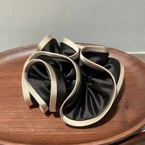Detail of a large satin scrunchie in black with champagne trim on a dark wood tray