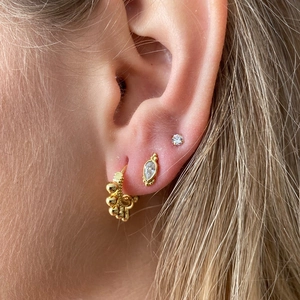 Macro view of gold hoop earring with round ball and sparkling waterdrop gemstone stud
