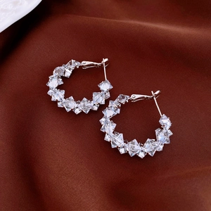 Close-up of silver hoop earrings with clear zircon crystals on dark silk fabric