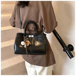 Détail du sac à main en cuir noir brillant avec surpiqûres et fermoir rotatif métallique