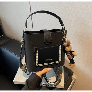 Detail of black bucket bag with gold rivets, embroidery strap and rabbit charm