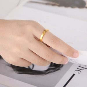 Close-up of a 3mm polished gold stainless steel flat ring worn on a hand over a magazine