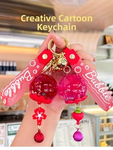 Close-up of creative liquid sand keychain with red and pink charms and golden bells