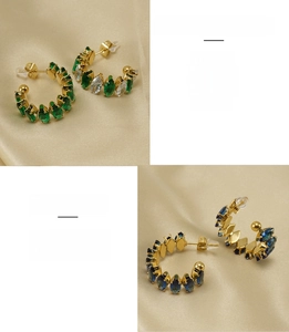 Dettaglio di orecchini a C in acciaio dorato 18K con pietre di zircone verde smeraldo e blu