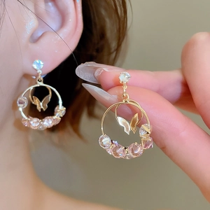 Detailed close-up of golden butterfly hoop earrings with pink and white zircon stones