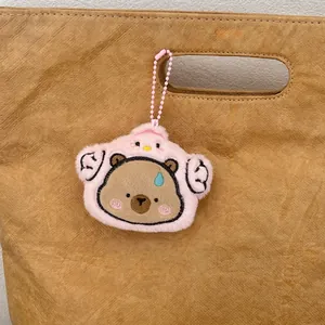 Süßer Capybara-Plüsch-Schlüsselanhänger im rosa Hühnerkostüm an einer braunen Handtasche