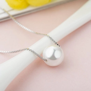 Macro shot of a minimalist white pearl pendant necklace with a silver box chain finish