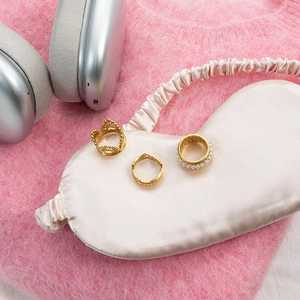 Close-up of 18K gold lace crown and pearl rings on soft champagne silk fabric