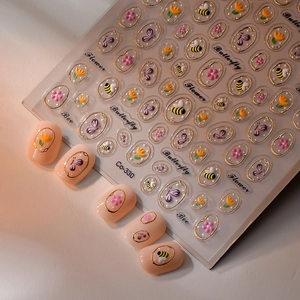 Détail de stickers à ongles 3D dorés avec motifs floraux et papillons sur ongles roses