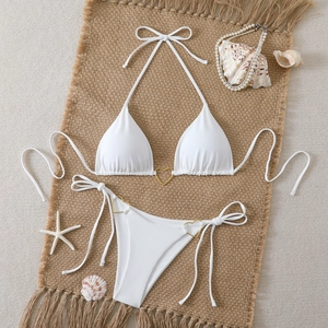 Close-up of white bikini with golden heart metal rings on a beach themed background