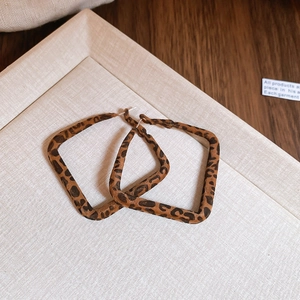Close-up of leopard print square earrings with silver needles on a linen tray