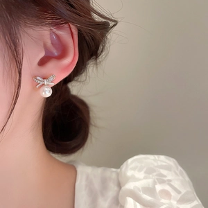 Gros plan d'une boucle d'oreille nœud en cristal avec une perle blanche sur l'oreille