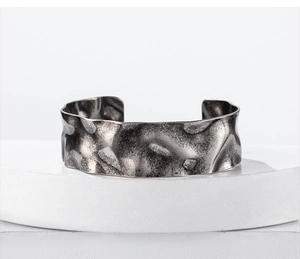 Macro detail of wide stainless steel cuff with hammered texture and vintage silver finish