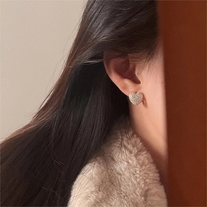 Close-up of elegant gold heart stud earrings featuring paved white zirconia on earlobe