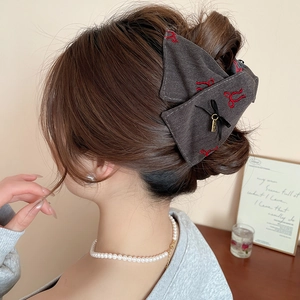 Detail view of a large dark grey fabric bow hair claw with red embroidery on a model