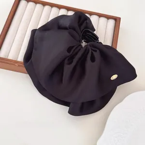 Close-up of a large black satin pleated hair claw clip with a gold metallic logo detail