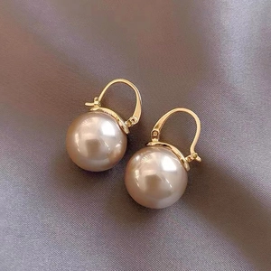 Macro shot of elegant champagne pearl drop earrings with golden metal hooks on silk