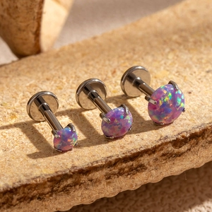 Three pieces of silver stainless steel labret studs with opal stones on stone surface
