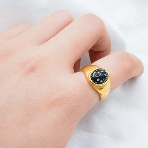 Detail of 18k gold plated signet ring with oval snowflake obsidian worn on index finger