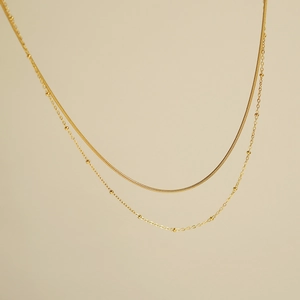 Detail of double-layer gold snake chain and satellite bead necklace in polished finish