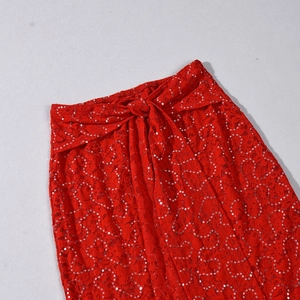 Detail of red lace dress with sequins featuring a bow tie waist and intricate texture