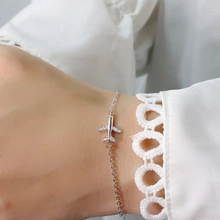 Detail view of a silver airplane pendant on a delicate chain worn with lace sleeves