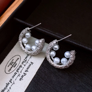 Detail of silver C-shaped earrings with pearls and zircons in a premium jewelry box
