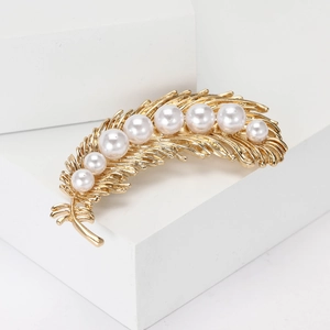 Elegant gold feather brooch with pearls displayed on a white stand for women's suits