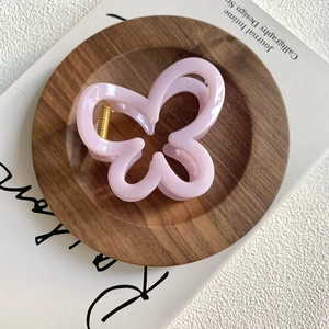 Close-up of pink butterfly hair claw clip with golden spring on a wooden tray