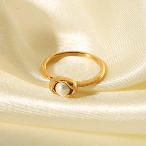 Nahaufnahme eines weißen Perlenrings in Goldfassung auf luxuriösem Champagner-Satin