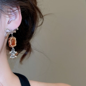 Close-up of asymmetric bow earrings with amber resin pendant and silver beaded fringe