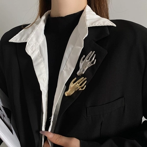 Detailed close-up of a stylish gold hand-shaped brooch on a black blazer lapel