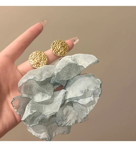 Detail of gold textured round stud earrings and light blue chiffon fabric flower accessory