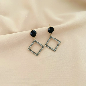 Elegant gold earrings with black round stones and diamond-set rhombus drop on beige cloth