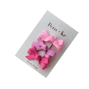Three-piece set of pink grosgrain ribbon bow hair clips on a white display card