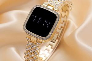Detail of square gold digital watch with crystal bezel on soft gold silk background
